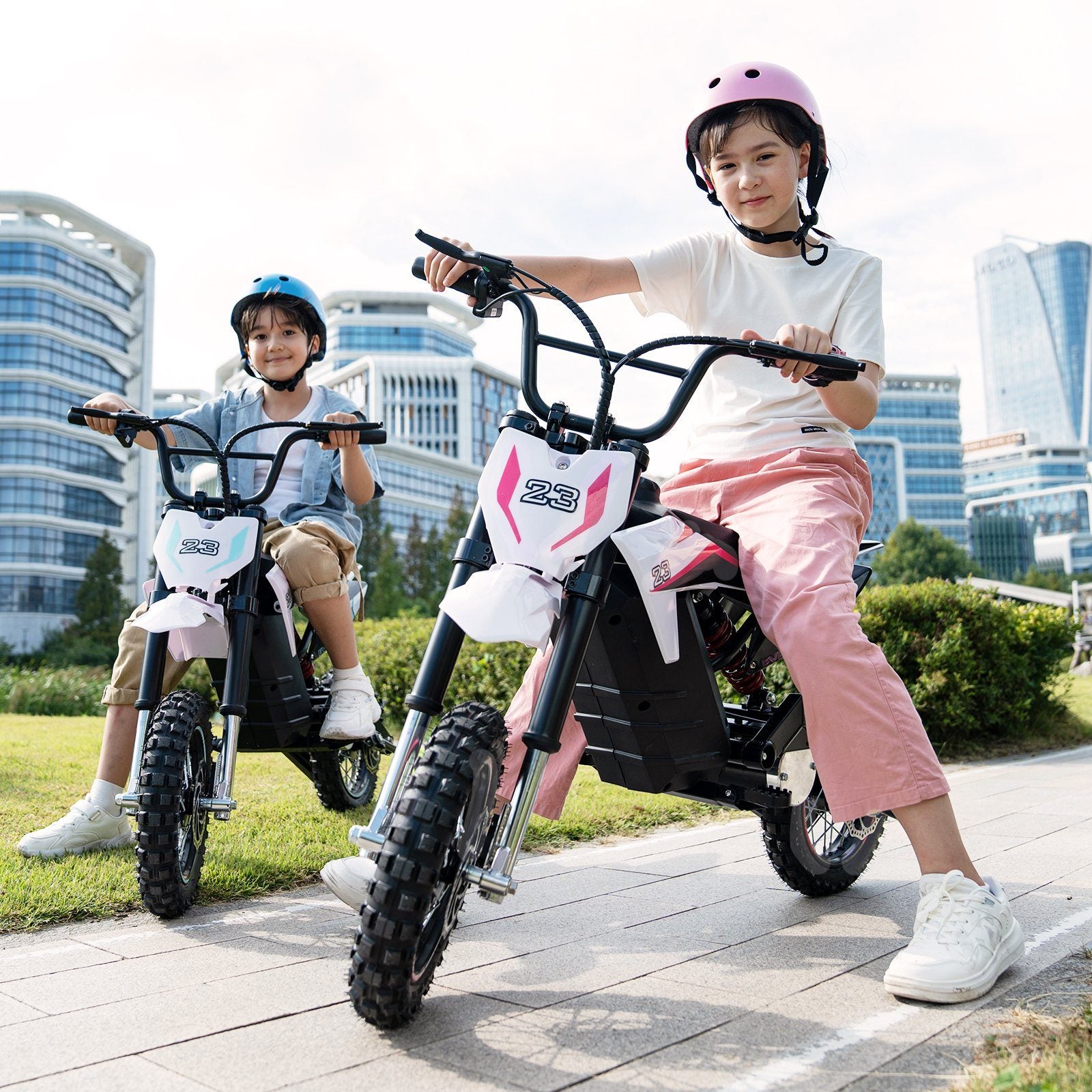 Zwei Kinder, die das EV65M Electric Kid Motorcycle fahren, eines in Blau und das andere in Pink, vor einem modernen städtischen Hintergrund.